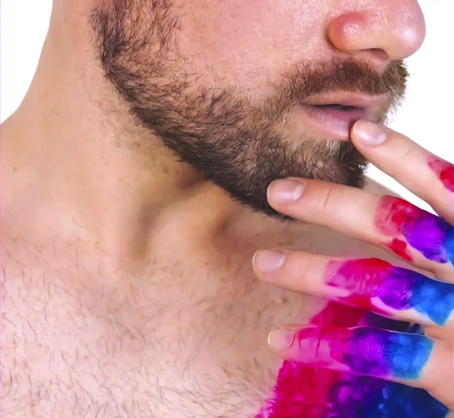 Close-up of a bearded man touching his lip with rainbow-painted fingertips