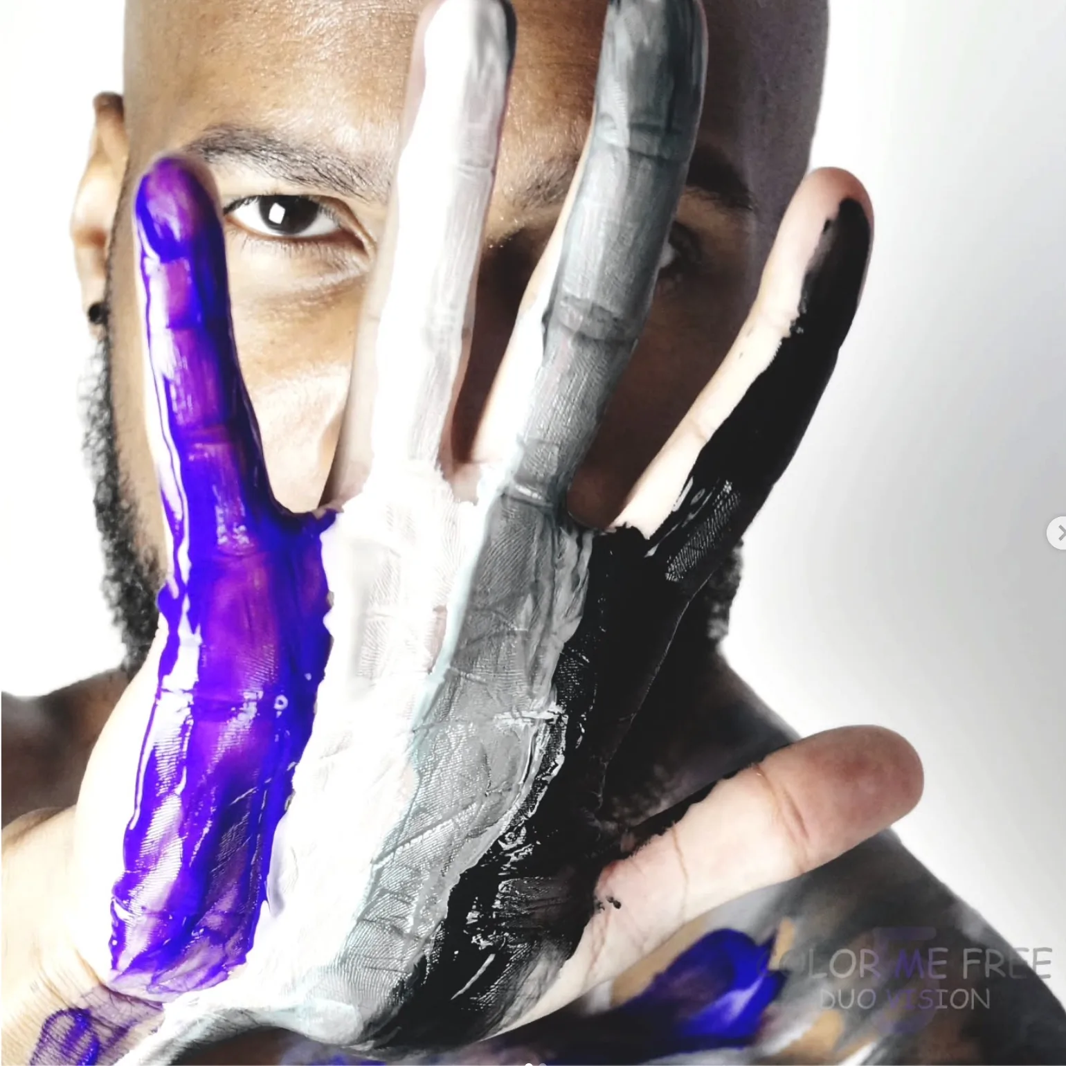Man covering half his face with a hand painted purple, white and black