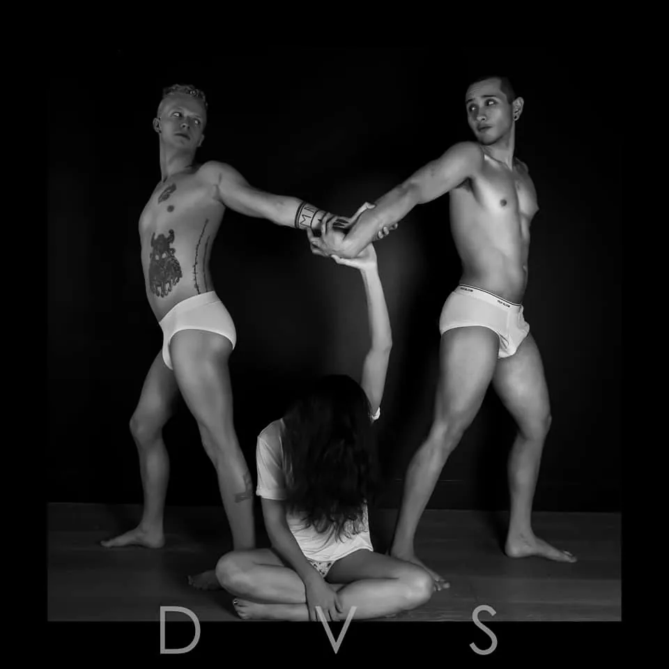 Two men forming an arch over a seated woman, black and white studio image