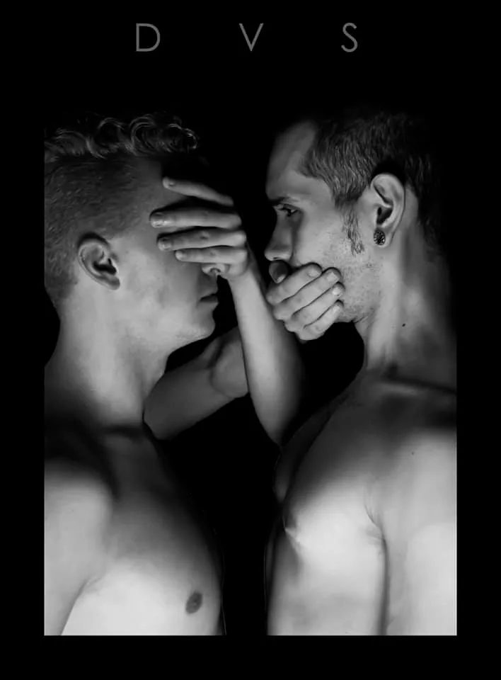 Black and white study of two men, one covering the other's eyes