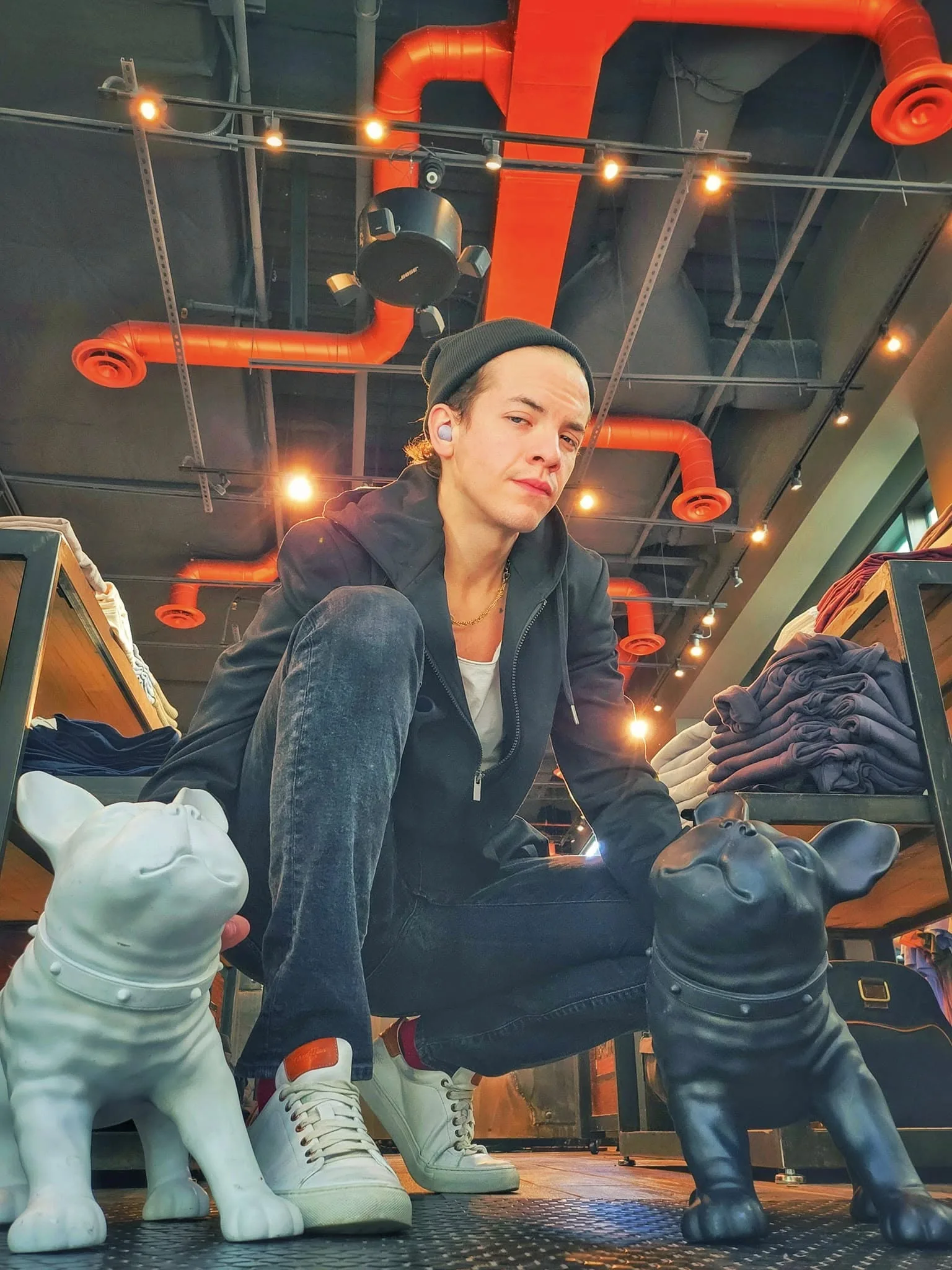 Gabriel Jasmer crouched between two statues in an industrial space