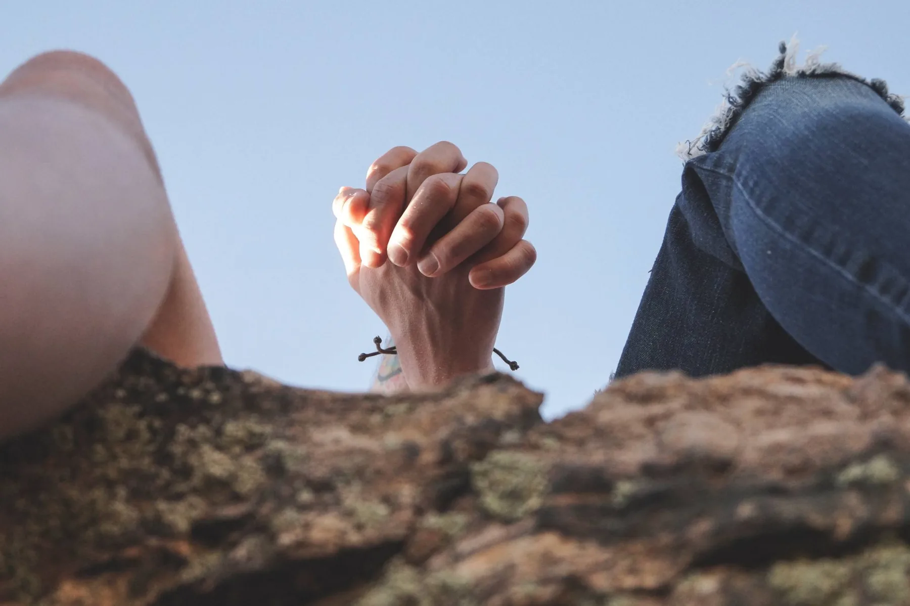 Couple's hands joined above a rock against a blue sky
