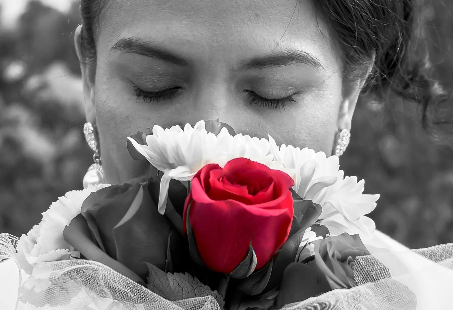 Woman with eyes closed holding a single red rose, black and white with selective color