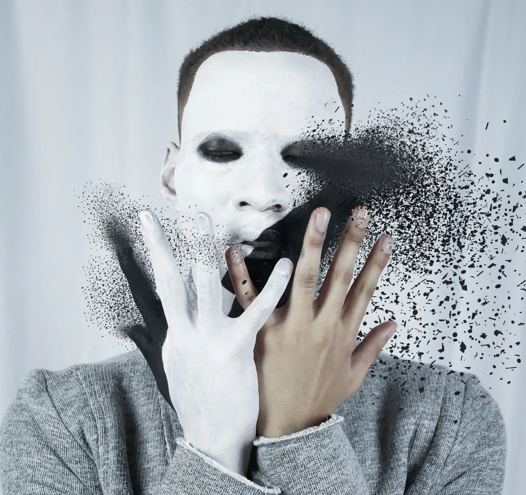 Man in white face paint dissolving into black particles